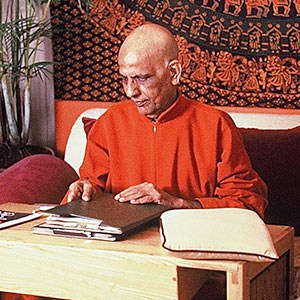 Swami Kripalvananda sitting at a desk holding a folder of papers..